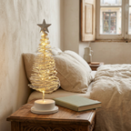 Árvore de Natal branca com luz LED acesa numa mesa de cabeceira, ao lado de um livro