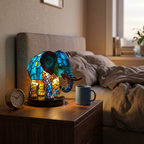 Candeeiro elefante com efeito vitral aceso numa mesa de cabeceira, com uma caneca e um despertador